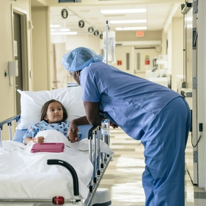 African male doctor holding hand of girl in hospital gurney.