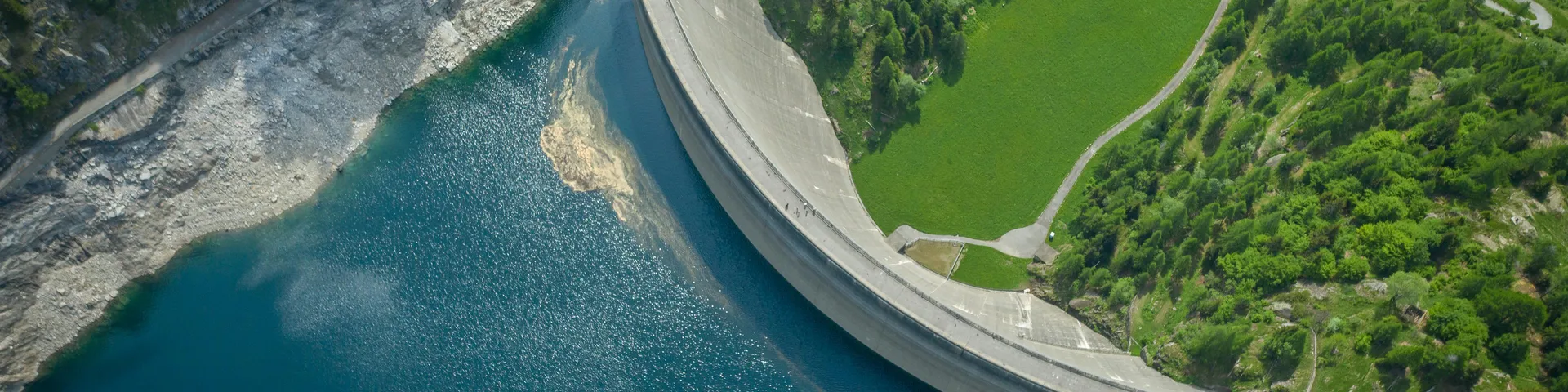 Green landscape surrounds the dam and water, country road visible below,