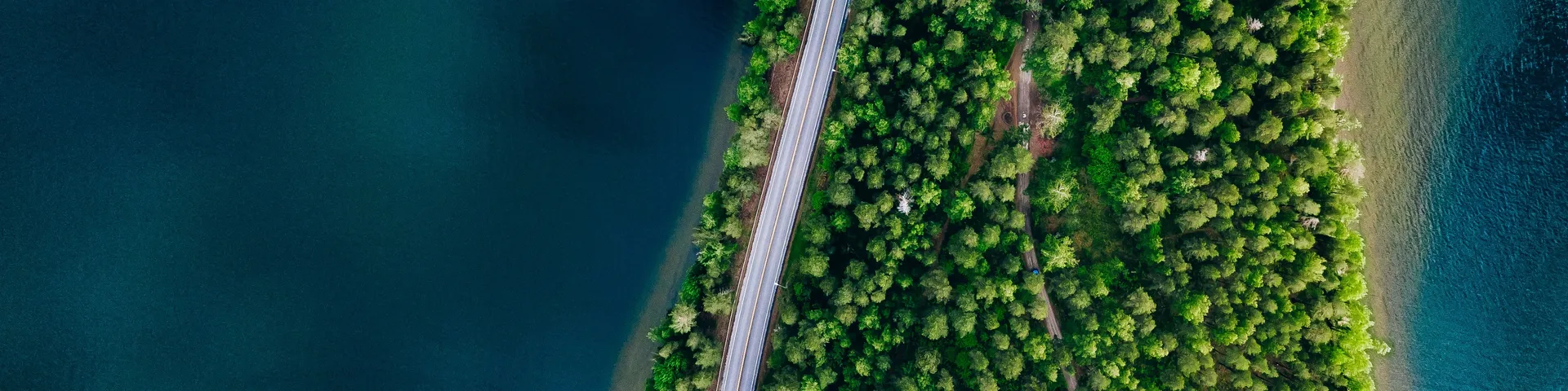 Aerial view of road between green forest and blue lake in Finland, 